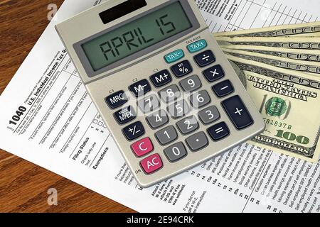 calculator with April 15 sign on hundred dollar bills and Internal Revenue Service 1040 income tax form Stock Photo