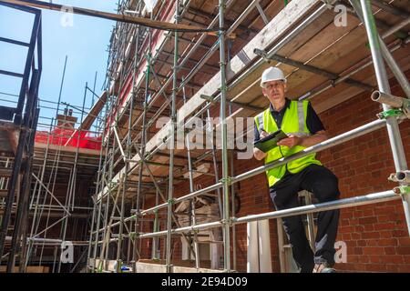 Male builder foreman, construction worker, contractor or architect on building site writing on black clipboard Stock Photo