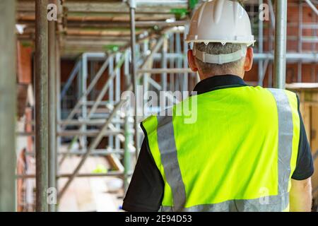 Rear view of male builder construction worker or builder on building site wearing hard hat and hi-vis vest Stock Photo