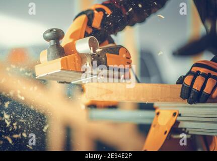 Caucasian Carpenter with Corded Wood Planer in His Hand Planing Wood Plank. Construction Site Theme. Stock Photo