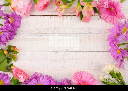 Frame of pink and purple flowers with rose, carnations, lilies and daisies against a white wood background. Copy space. Stock Photo