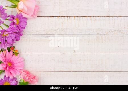 Side border of pink and purple flowers with rose, carnation and daisies against a white wood background. Copy space. Stock Photo
