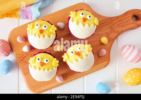 Hatching spring chick cupcakes on a wood paddle board. Flay lay against a white wood background. Stock Photo