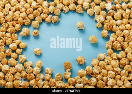 Popcorn is scattered on a blue background, in the form of a frame. Yummy for the filming of movies, TV series, cartoons. Free space, top view Stock Photo