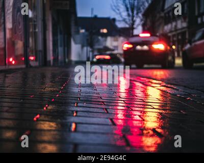 Selective focus of a paved path reflecting car lights on a rainy day in the evening Stock Photo