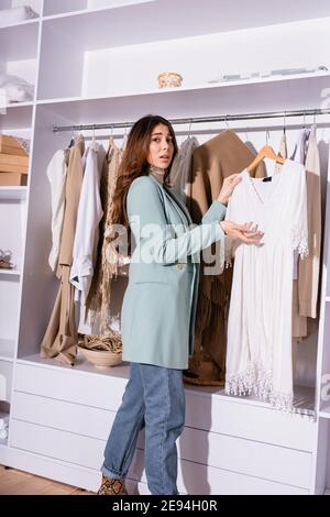 Confused woman pointing at dress on hanger in wardrobe Stock Photo