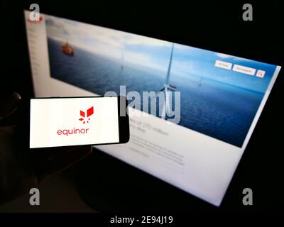 Person holding smartphone with logo of Norwegian energy company Equinor ASA on display in front of business website. Focus on phone screen. Stock Photo