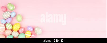 Easter banner with pastel colored egg corner border over a pink wood background. Top view with copy space. Stock Photo