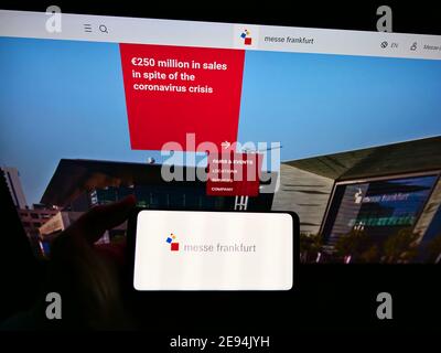 Person holding mobile phone with logo of German trade fair company Messe Frankfurt GmbH on display in front of website. Focus on cellphone screen. Stock Photo