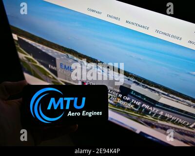 Person holding smartphone with logo of German aircraft engine manufacturer MTU Aero Engines AG on display in front of website. Focus on phone screen. Stock Photo
