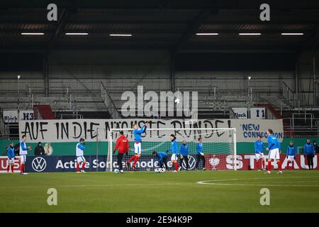 Kiel, Germany. 02nd Feb, 2021. Football: DFB Cup, Round of 16, Holstein Kiel - Darmstadt 98, at Holstein Stadium. Kiel's players are warming up before the game. A poster with the text 'On to the next round' hangs in the stands. Credit: Christian Charisius/dpa - IMPORTANT NOTE: In accordance with the regulations of the DFL Deutsche Fußball Liga and/or the DFB Deutscher Fußball-Bund, it is prohibited to use or have used photographs taken in the stadium and/or of the match in the form of sequence pictures and/or video-like photo series./dpa/Alamy Live News Stock Photo
