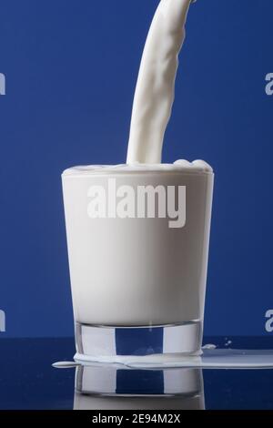 Close-up bottle of milk pouring into a glass to the brim and isolated on blue background Stock Photo