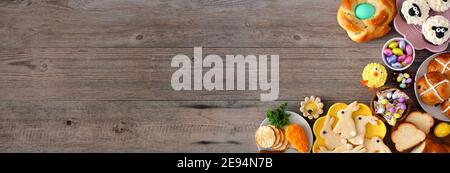 Easter table scene with a selection  of breads, desserts and treats. Top view banner with corner border over a wood background. Stock Photo