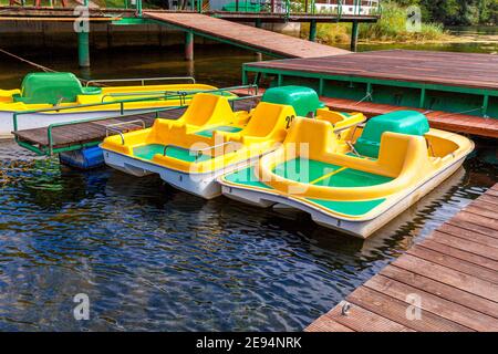 Pedal boats or paddle boats catamarans station. Yellow water bicycles locked at lake marina dock pier on sunny summer day. Summer leisure activity out Stock Photo