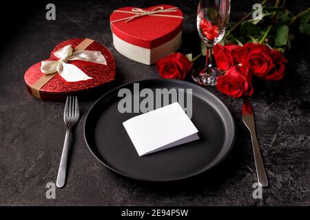 Valentines day or birth day celebration dinner concept with an empty black matte plate, hearth shaped gift box and red roses Stock Photo