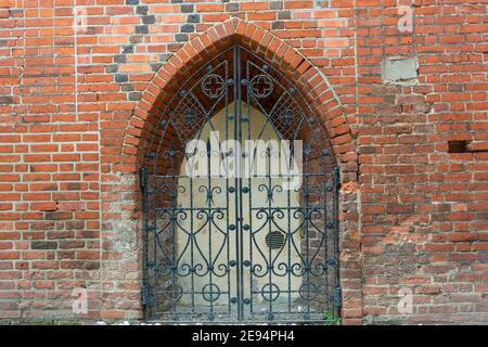 Forged iron gates on wall of an old brick castle. An arch-shaped door, ancient architecture of Europe. Stock Photo
