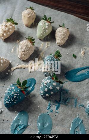 Step by step. Tasty Blue and white chocolate dipped strawberries with sugar sprinkles on a parchment paper Stock Photo