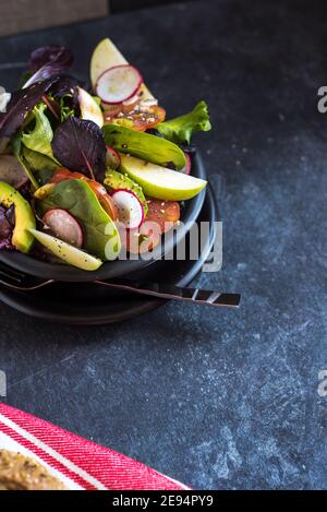 delicious tomato and guacamole lettuce salad, with green apple and radish decorated with flax seeds, on dark background Stock Photo