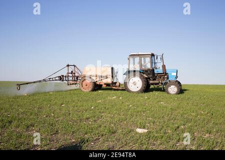 Farmer on a tractor is spraying green wheat field. Beautiful views of Moldova. Stock Photo