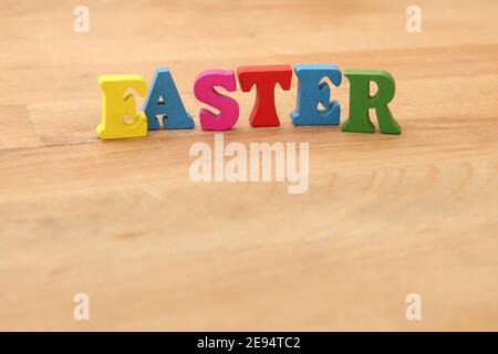 Easter spelt in colourful wooden letters against a natural wooden beige background. Stock Photo