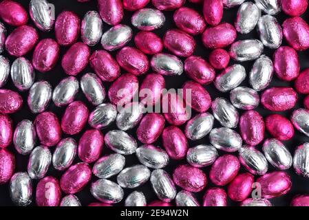 Pink and silver foil wrapped chocolate easter eggs, against a black background. Stock Photo