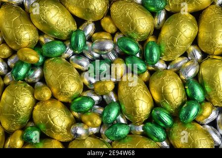 Large & small yellow, gold, green and silver spring colours of foil wrapped chocolate easter eggs, against a black background. Stock Photo