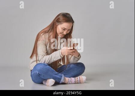 a girl with a phone in her hands sits on a white background smiling Stock Photo