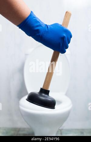 Hand in gloves holding suction cup with toilet bowl blurred on background. Stock Photo