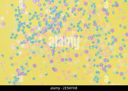 Festive yellow background with colorful flowers. Multi-colored small artificial flowers. Flat lay, top view. Stock Photo