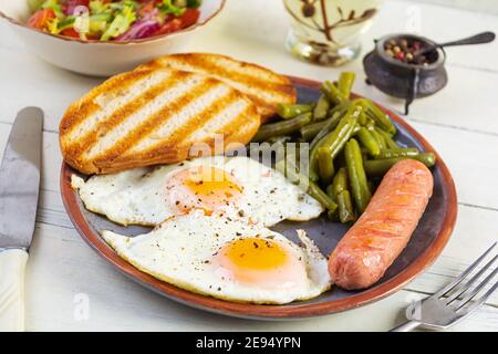Breakfast with eggs, grilled sausage, green beans and toast on wooden background Stock Photo