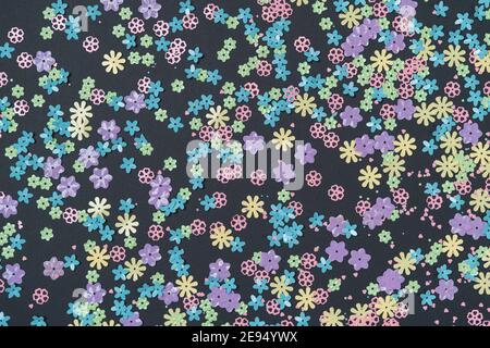Festive black background with colorful flowers. Multi-colored small artificial flowers. Flat lay, top view. Stock Photo