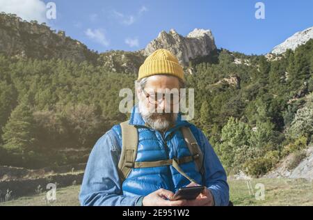 Portrait of a bearded explorer man walking through the mountains, using the map of his mobile phone Stock Photo