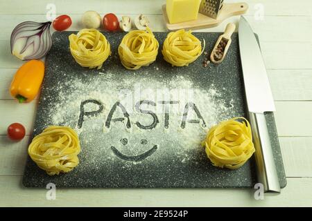 Pasta and vegetables on the table as a background with space for text. Pasta background. Assorted dry pasta with vegetables on a wooden table. Free sp Stock Photo