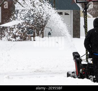 Selective focus on a snow blower shooting the now off of a driveway on to the street after a snow storm on Long Island. Stock Photo