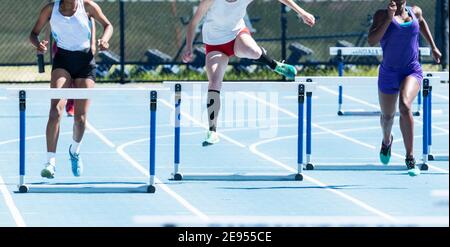 Three high school girls competing in a four hundred meter hurdle race on an outdoor track in the summer. Stock Photo