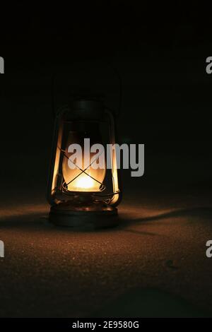 An old kerosene lamp with a lit fire stands on the snow-covered ground outdoors on a winter night. Cozy warm yellow light of an old kerosene lamp. Stock Photo