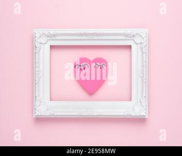 Heart shape pink paper with eyelashes  in frame on pink background. Valentines or woman's day background design. Minimal flat lay. Stock Photo