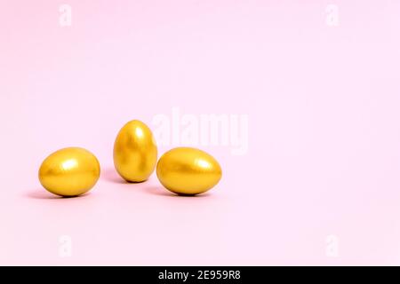 Three Easter eggs decorated with gold paint on a pink background. Concept for Easter, spring. Selective focus. Copy space. Stock Photo