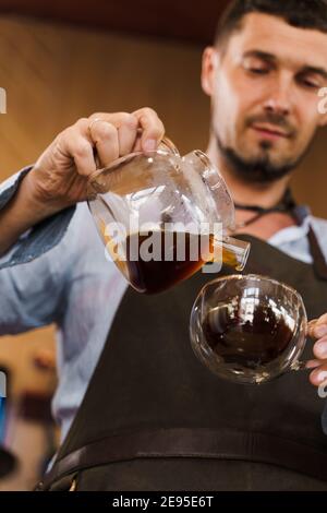 Close-up pouring coffee in double glass cup in cafe by handsome bearded barista. Coffee brewing syphon and aeropress alternative methods. Advert for s Stock Photo