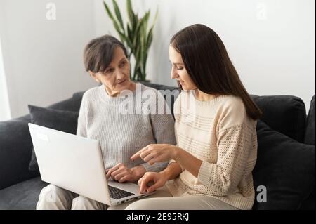 An adult daughter is teaching to senior mother how to pay bill online, web searching, explains to mature mom how use computer, helps send email Stock Photo