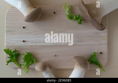 Eringi mushrooms with lettuce leaves on a wooden cutting board on a pastel background. Pleurotus eringi. Healthy food concept. Horizontal orientation. Stock Photo