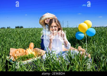 Three happy kids sitting on picnic on the field. blue sky, green grass. bread, pies and fruits in a basket. Stock Photo