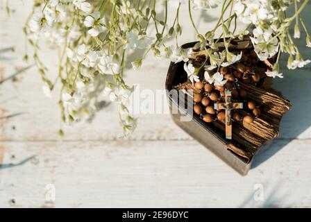 Hands folded in prayer over old Holy Bible. Wooden background.Hands and rosary, prayer, book with yellow pages. white flowers on a background. in the Stock Photo