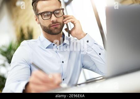 Calm concentrated manager listening to his client on the phone and making notes Stock Photo