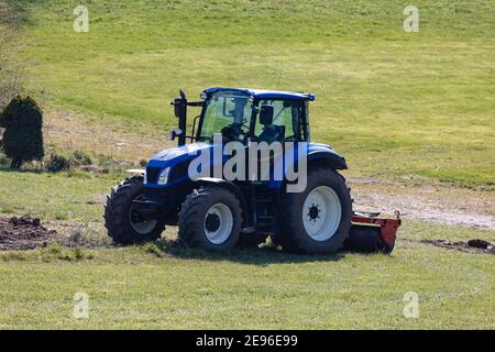 blue tractor ready for field work but without driver on a green meadow, photographed from front side, on day without people Stock Photo