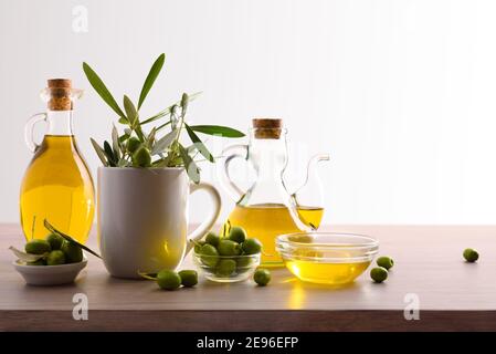 Virgin olive oil in two glass containers and harvest olives on the wooden bench white isolated background. Front view. Stock Photo