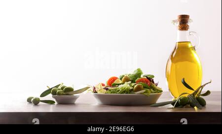 Virgin olive oil in two glass containers and harvest olives on the wooden bench white isolated background. Front view. Stock Photo