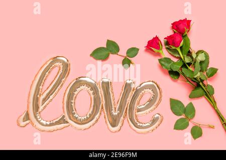 Golden foil balloon in shape of Love word and three red roses bouquet on pink background. Love and dating concept. Mothers, Valentines day or wedding Stock Photo