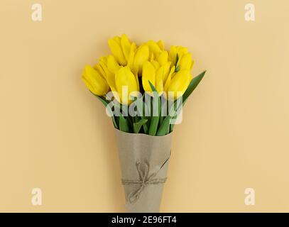 Bouquet of yellow tulips wrapped in craft paper on beige background. Stock Photo