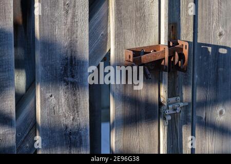 A rusted metal latch holds the gate of a wooden fence shut. Stock Photo